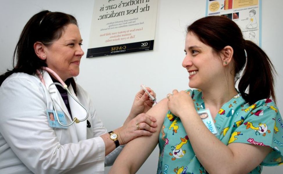 Large photograph depicted an adult female healthcare professional as she was receiving an intramuscular vaccination 725x479
