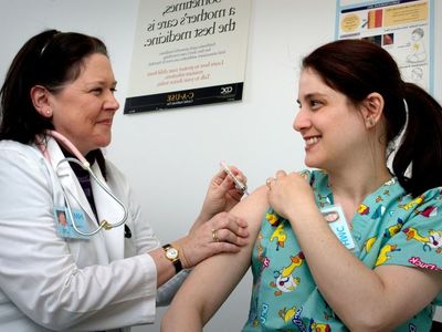Medium photograph depicted an adult female healthcare professional as she was receiving an intramuscular vaccination 725x479